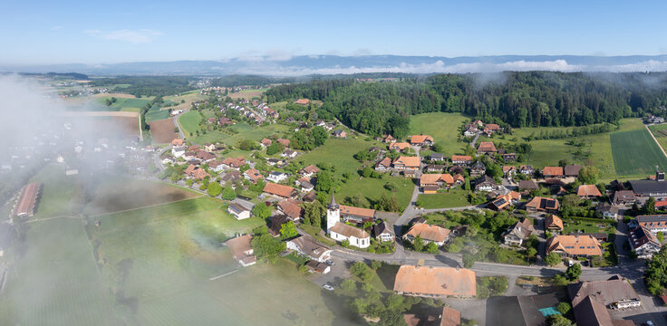 Aerial view of the village of Grossaffoltern with its historic church, traditional houses, and surrounding green fields under a light morning mist Grossaffoltern, Canton of Bern, Switzerland.