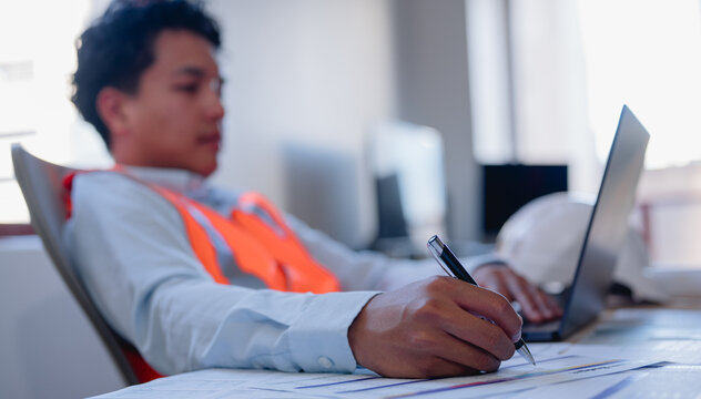 Male engineer using computer laptop and pen working on site analytic data charts for workflow and programming.