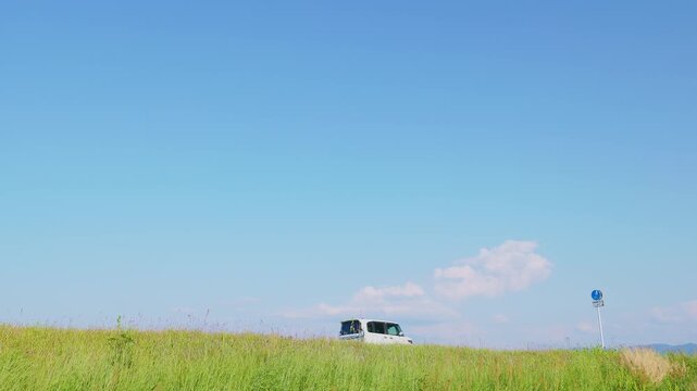 青空と緑の堤防を走る白い軽自動車（福岡県小郡市）