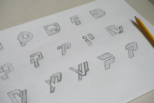 Pencil-drawn symbol and logo concepts are sketched across a dotted sheet of paper beside a yellow pencil.