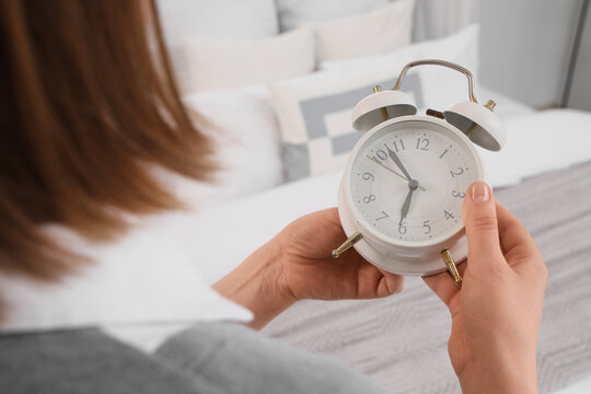 Woman setting time on alarm clock in bedroom, closeup. Daylight saving time concept