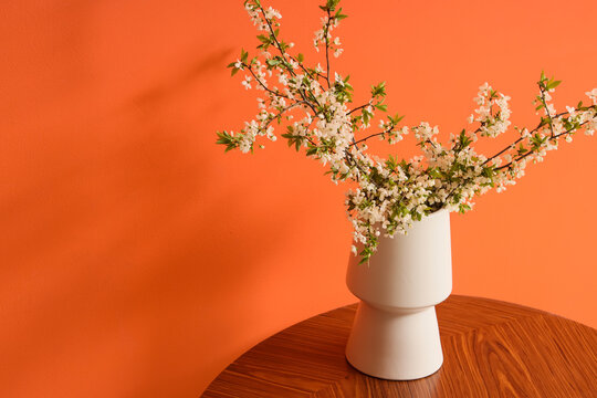 Vase with blooming tree branches on table near orange wall, closeup