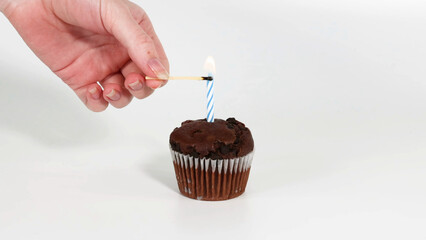 Obraz premium Hand Lighting a Blue Striped Candle on a Chocolate Cupcake