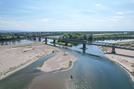 Aerial view of the historic Ponte della Becca iron truss bridge crossing the river Po with exposed sandbanks and green trees in Linarolo, Lombardia, Italy.