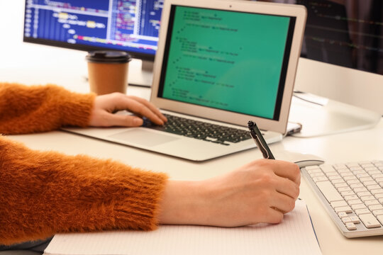 Female programmer's hands working with laptop and notebook on table in office