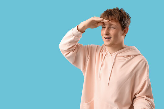 Young man looking far away with hand over head on blue background