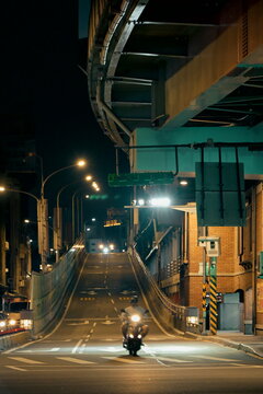 Taipei, Taiwan - Nov 22, 2025: Motorcycle riding under Taipei Bridge ramp with elevated concrete structure, street lights and urban road markings at night.