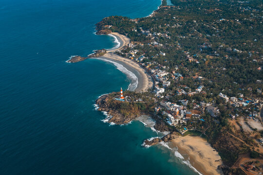 Aerial view of Vizhinjam Lighthouse on a rocky headland overlooking sandy beaches and the Arabian Sea in Kovalam, Kerala, India.