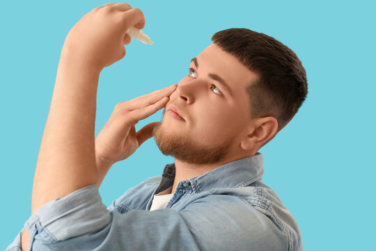 Young man applying nasal spray for allergy relief and sinus treatment isolated on blue background, closeup portrait of male using medicine for cold, flu or congestion
