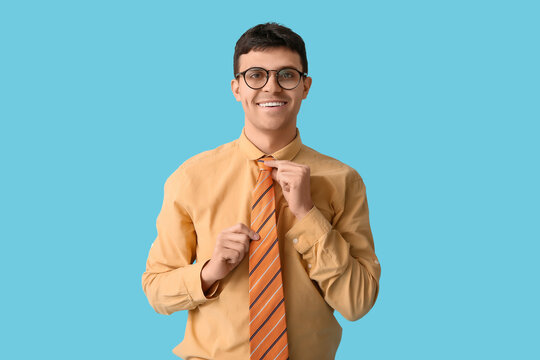 Happy young man straightening his tie on blue background