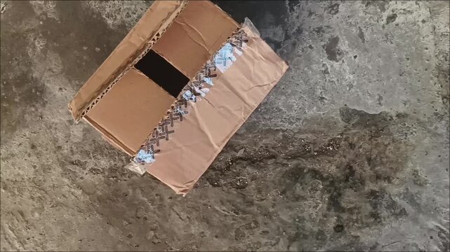 Crumpled and ripped brown delivery package package on textured concrete ground. Stock footage of damaged logistics