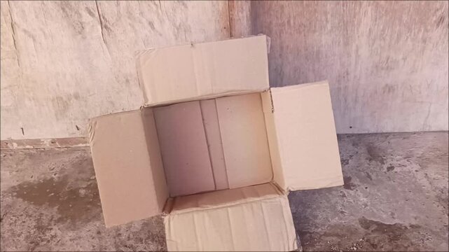 High angle shot of an empty open cardboard box with extended flaps on a rustic concrete floor