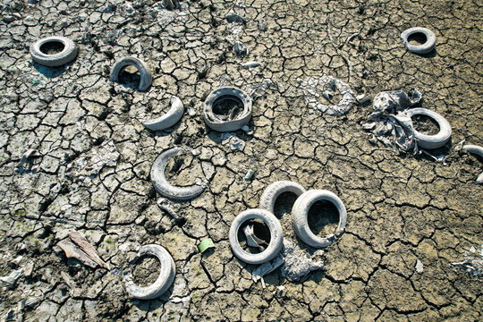 Aerial view of discarded old tires scattered across parched and cracked dry earth during a severe drought Carignano, Piemonte, Italy.