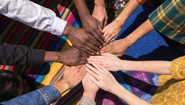 Diverse group of people from different ethnic backgrounds putting their hands together in a symbol of unity and teamwork on a colorful fabric