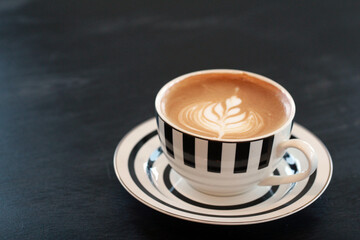 Obraz premium Hot latte with elegant latte art in a black and white striped cup, cafe beverage concept.