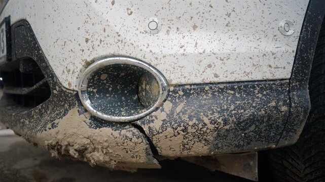 Close up of a dirty white vehicle bumper covered in dried mud, splashes, and road grime