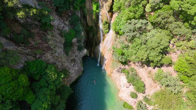 Top Down Aerial View of Polylimnio Waterfall and Turquoise Natural Pool Surrounded by Forest and Rocky Canyon in Greece