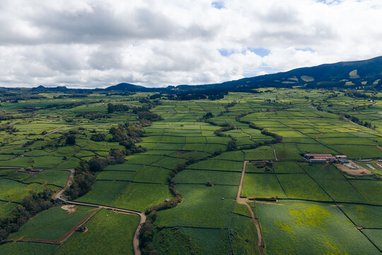 Aerial view of the green patchwork fields and stone walls of Terceira Island under a cloudy sky in Azores, Portugal.