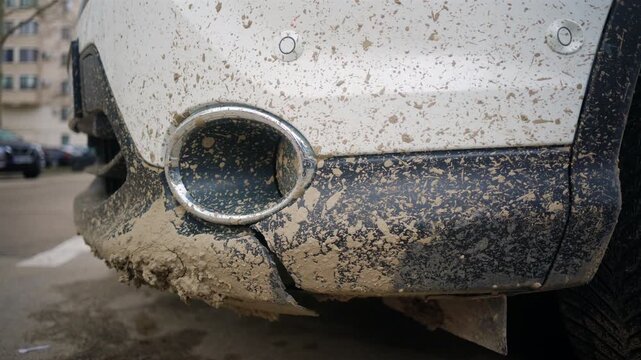 Close up of a dirty white vehicle bumper covered in dried mud, splashes, and road grime