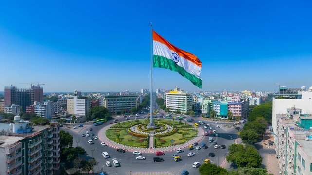 Aerial view of a large Indian flag flying over a busy city roundabout with modern buildings and clear blue sky