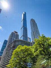 Obraz premium Low angle view of modern skyscrapers over green trees in Manhattan. Modern residential skyscrapers including Central Park Tower rising above green deciduous trees in New York City.