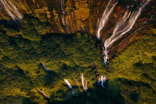 Aerial view of Poco da Ribeira do Ferreiro waterfalls cascading down a steep mossy cliff into lush vegetation during golden hour Fajazinha, Azores, Portugal.