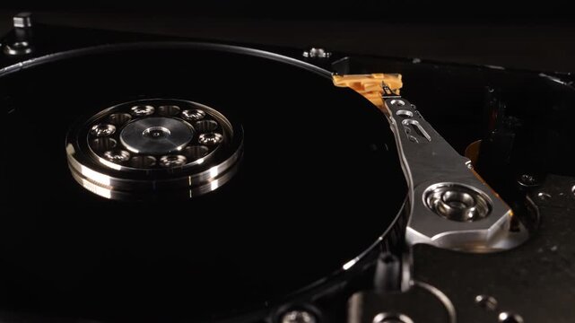 Closeup shot of the inside of a hard drive. Different components. The disk is spinning. Metallic. Technology. Storage. Blurred background. Selective focus. Camera slowly moving around.