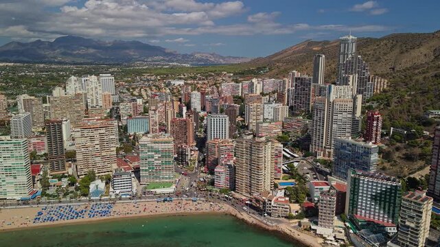 Aerial panorama of benidorm city, skyscrapers with beach and mountains in background, dynamic coastal landscape footage.