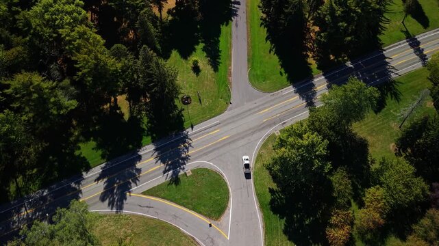 Aerial view of car turning right at three-way intersection surrounded by trees on a sunny day.