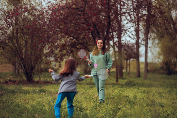 Fototapeta premium Happy Mom and Little Girl Playing Badminton Outdoors. Person texting message networking online on her mobile phone 