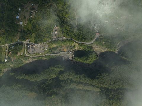Aerial view of Tambang Pasir Merapi Kali Gendol Sand Mine with a deep ravine, lush vegetation, and a winding road in Kecamatan Cangkringan, Daerah Istimewa Yogyakarta, Indonesia.