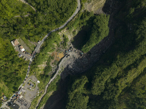 Aerial view of Tambang Pasir Merapi Kali Gendol Sand Mine with heavy machinery and trucks surrounded by lush green forest in Kecamatan Cangkringan, Daerah Istimewa Yogya, Indonesia.
