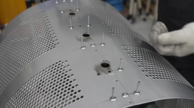 Worker inserting metal rivets into perforated stainless steel washing machine drum bottom plate at workbench