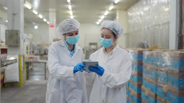Food Safety Inspection: Two dedicated professionals, dressed in protective gear, meticulously inspect production details with modern tech in a clean food processing facility.
