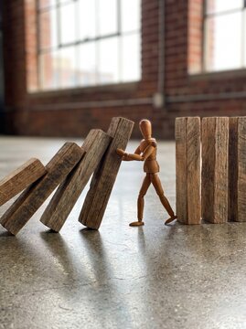 A wooden mannequin heroically attempts to halt a domino effect of falling wooden planks