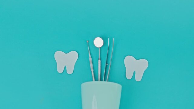 Minimalist Dental Flat Lay With Plastic Cup Holding Steel Tools Placed Between Two Paper Teeth Cutouts On Teal Background