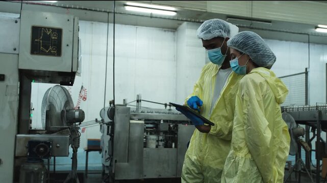 Two industrial engineer supervisors examine and inspect quality on factory conveyor belt machine, check production process in canned food manufacture, and protective uniforms for hygiene operations.