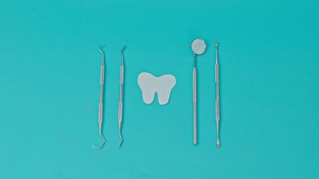 Top-Down View Of Professional Dental Instruments As Dentist Hand Sets Down Paper Tooth Icon On Turquoise Background