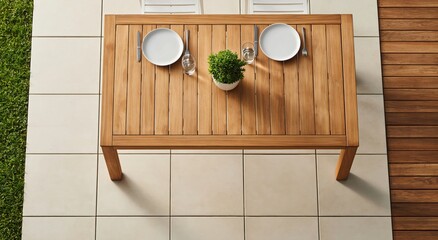 Naklejka premium Overhead view of rectangular wooden dining table set for two on tiled patio, featuring two plates and small potted plant.