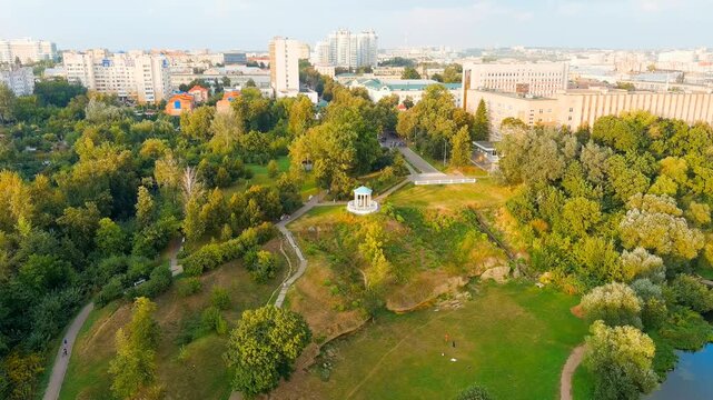 Oryol, Russia. The white rotunda of Dvoryanskoe Gnezdo Park, a classical gazebo perched on a grassy hilltop amid dense summer foliage, aerial descent view toward the pavilion. Drone footage