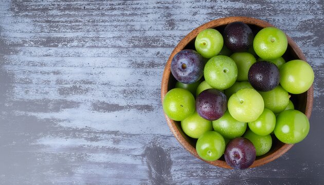 Fresh green greengage plums and purple plums with water drops in wooden bowl on rustic background top view copy space