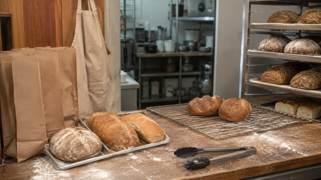 Rustic bakery bread counter real life scene artisan loaf fresh bread bakery kitchen flour dust cooling rack paper bag metal tong crust sourdough