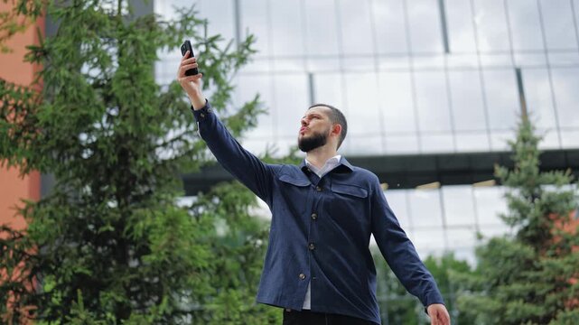 Shocked man reading unexpected news or error on mobile phone near office building. Concept of bad news, financial loss, technical problem or surprising message.
