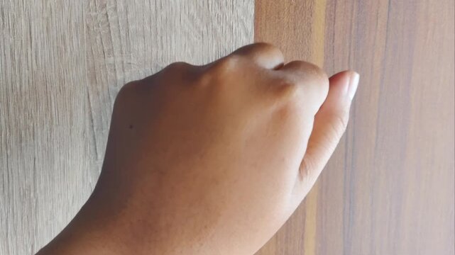Close up of a hand knocking on a wooden door, symbolizing waiting or visiting.