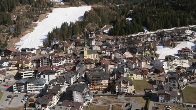 Village Of Ischgl In Tyrol, Austria, With Green-spired Church And Ski Resort On Sunny Day. aerial tilt-up shot