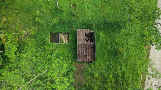 Aerial view of a ruined house with a collapsed roof and overgrown vegetation in Cangkringan, Special Region of Yogyakarta, Indonesia.