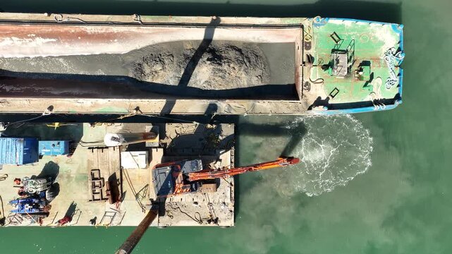 Sand dredging and digger at work on barge and work platform at harbour - drone view