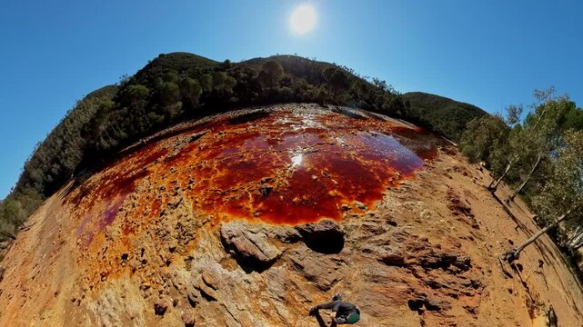 Reddish orange acidic water flowing through a mining area, forming an unusual and contaminated environment under a clear sky