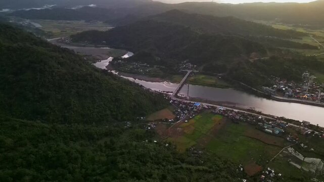 Aerial drone shot of Guinobatan in Bato, Catanduanes with lush mountain terrain, bridge crossing, and rural village communities during sunrise