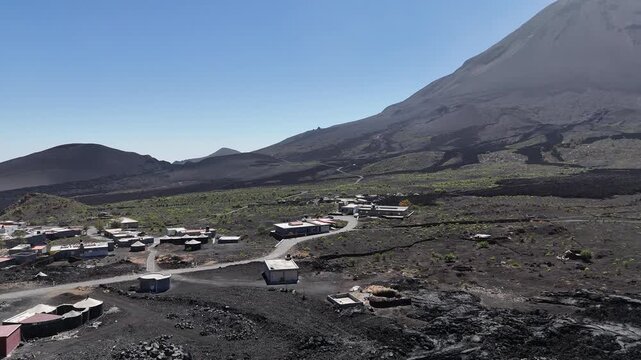 Aerial view of the remote Ch&atilde; das Caldeiras village at the foot of Fogo Volcano in Cabo Verde, featuring low-rise buildings nestled within the dark, expansive volcanic landscape